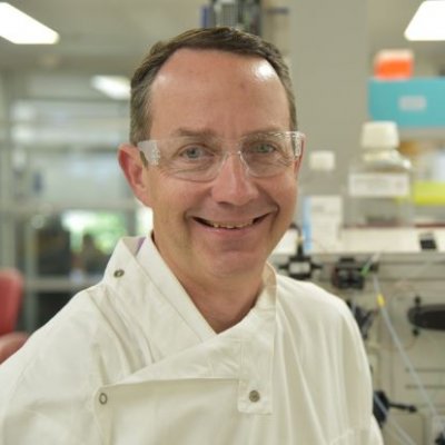 Portrait photo of UQ Professor Trent Munro wearing a white coat in a laboratory. Supplied.